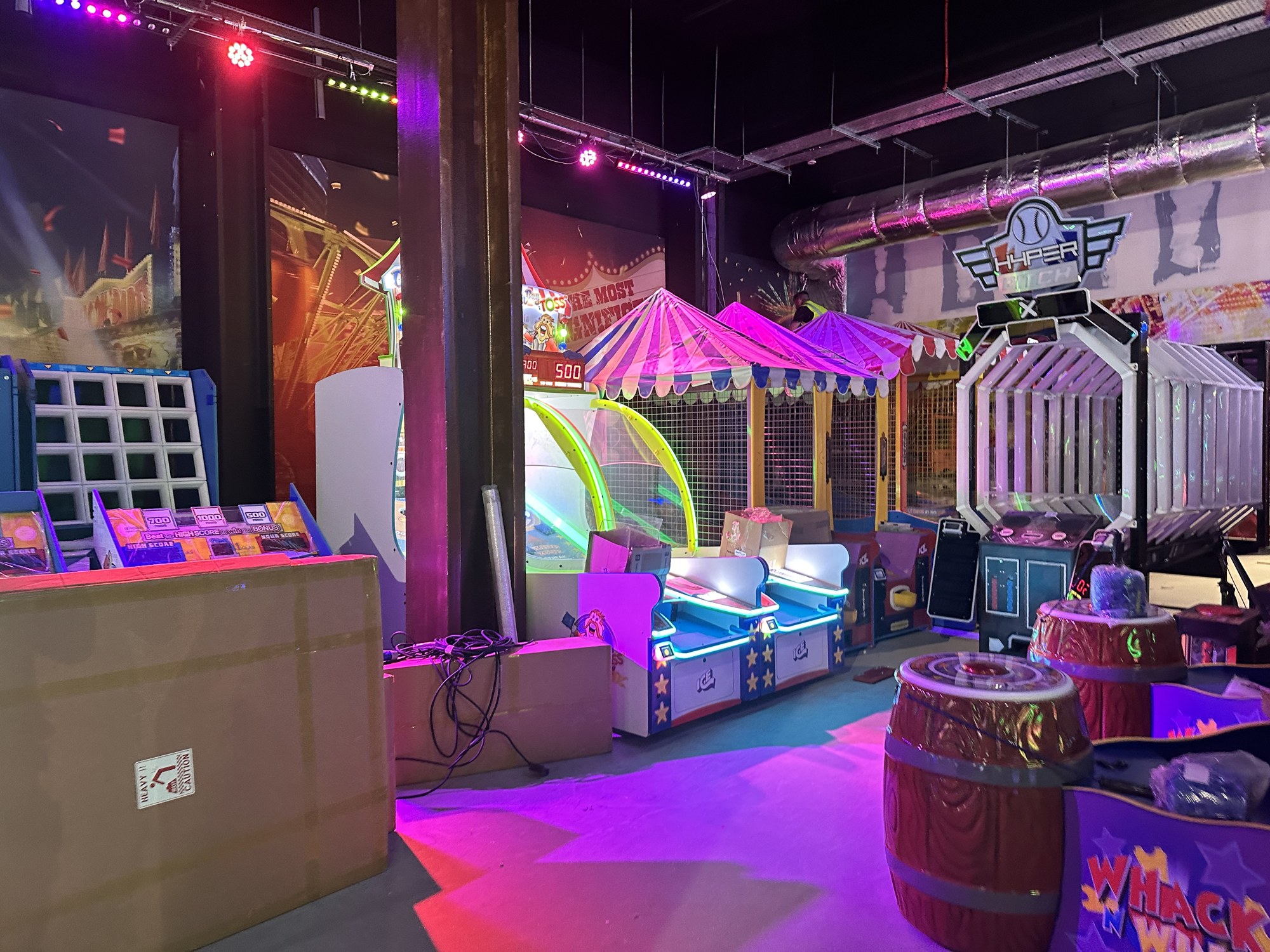 Wide view of a commercial leisure venue fit-out with fairground games, feature lighting and exposed ductwork overhead